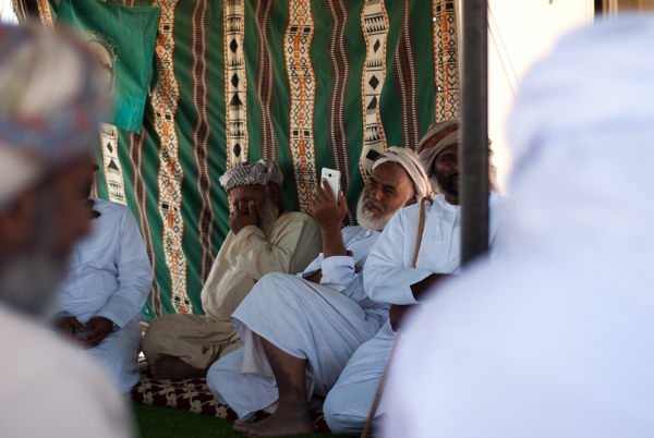 Man awaiting arrival of guests - viewing short video of welcome qasida on smart phone
